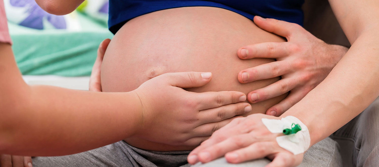 Hände tasten Bauch einer schwangeren Frau ab. 