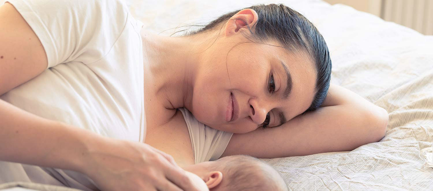 Nahaufnahme: Mutter stillt Neugeborenes im Bett. 