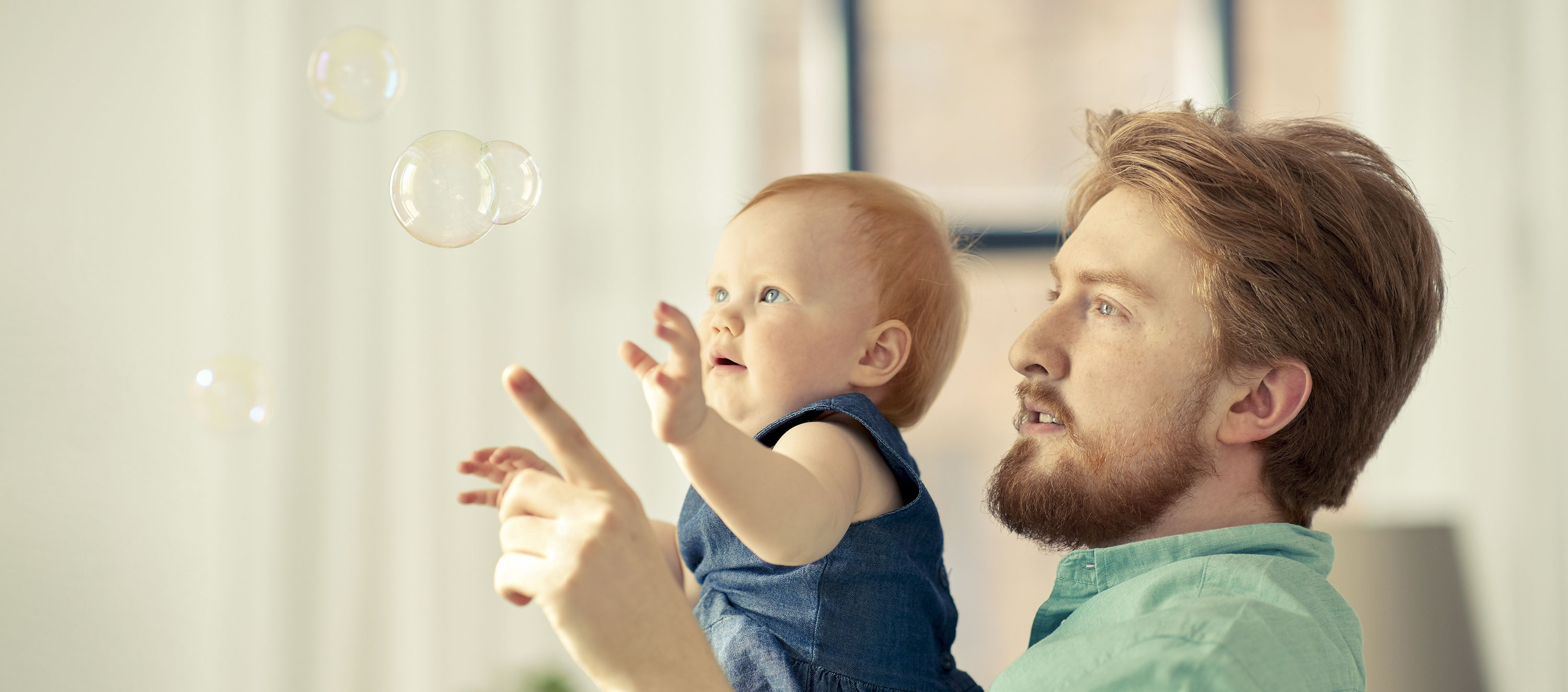 Vater und Kleinkind betrachten Seifenblasen. 